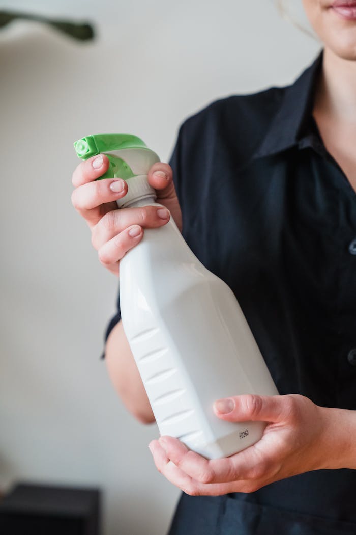 Close-up of a person holding a white spray bottle with a green nozzle, indoors.
